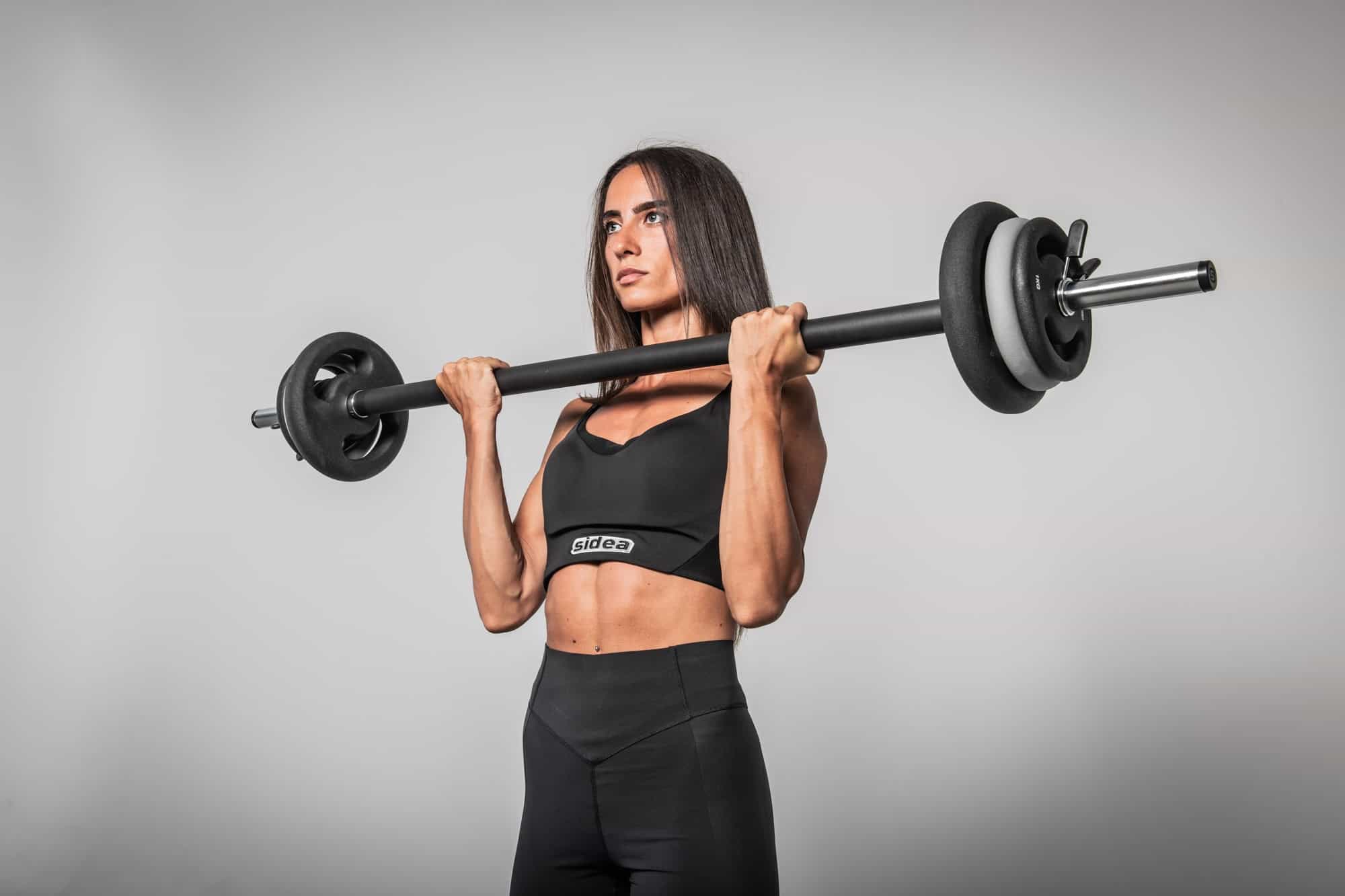 Woman performing overhead press with a Sidea SuperPump kit and studio barbell